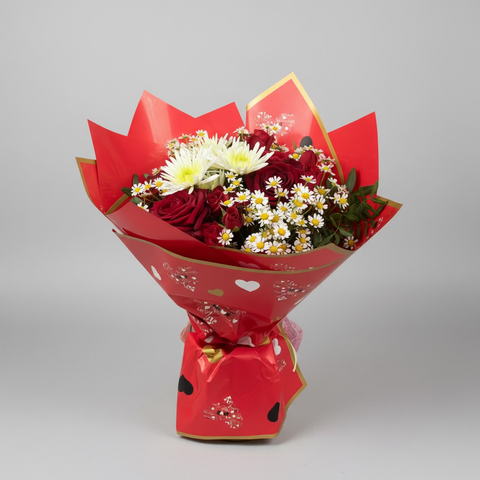 Bouquet of flowers wrapped in red paper on a counter with various items in the background.