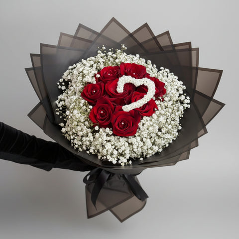 Bouquet of red roses with a heart-shaped arrangement on top, surrounded by baby's breath.